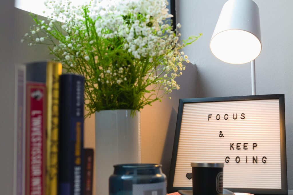 A cozy office space featuring books, a vase with flowers, lamp, and motivational sign.